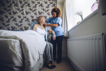 caregiver dressing her patient in bed